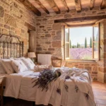 Chambre authentique dans une ferme en pierre de Provence avec poutres apparentes, carrelage en terre cuite et vue sur les champs de lavande