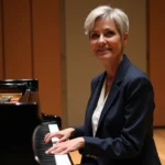 Chanteuse Stone assise devant un piano à queue dans un studio d'enregistrement professionnel, reflet de son parcours artistique en 2026